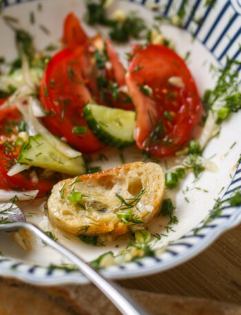 Fresh tomato cucumber salad with dill, onion, and olive oil served in a bowl with bread.