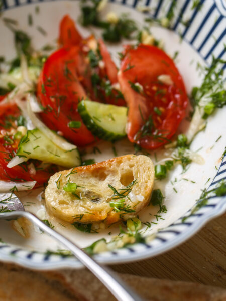 Fresh tomato cucumber salad with dill, onion, and olive oil served in a bowl with bread.