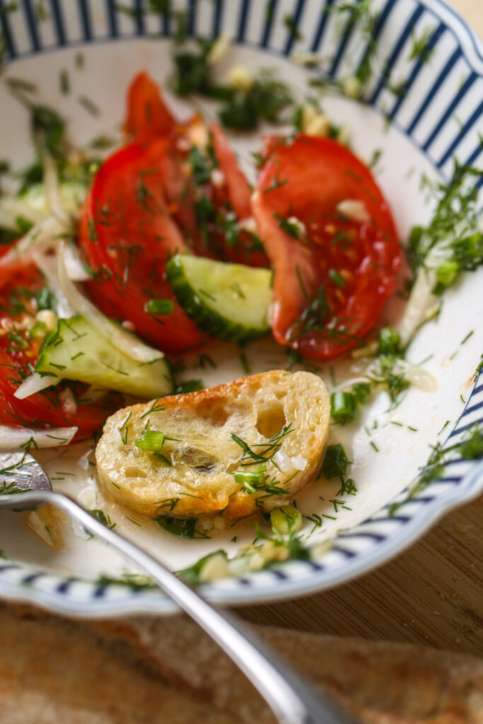 Fresh tomato cucumber salad with dill, onion, and olive oil served in a bowl with bread.