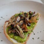 Avocado toast topped with soy sauce glazed mixed mushrooms and fresh parsley on rustic sourdough.