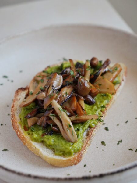 Avocado toast topped with soy sauce glazed mixed mushrooms and fresh parsley on rustic sourdough.