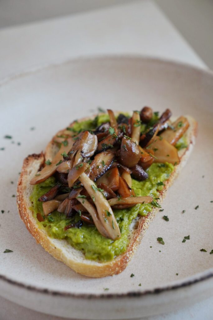 Avocado toast topped with soy sauce glazed mixed mushrooms and fresh parsley on rustic sourdough.