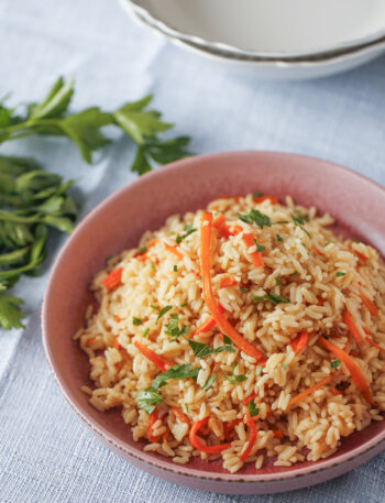 Fluffy carrot and onion pilaf with parboiled rice garnished with fresh parsley