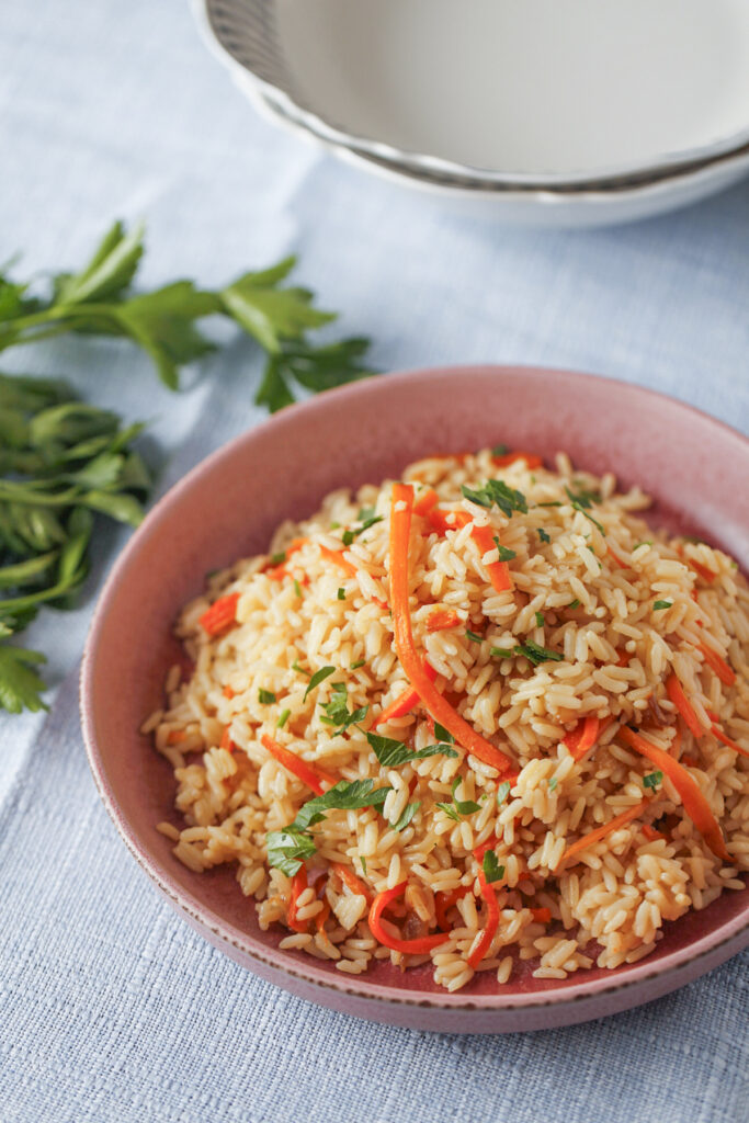Fluffy carrot and onion pilaf with parboiled rice garnished with fresh parsley