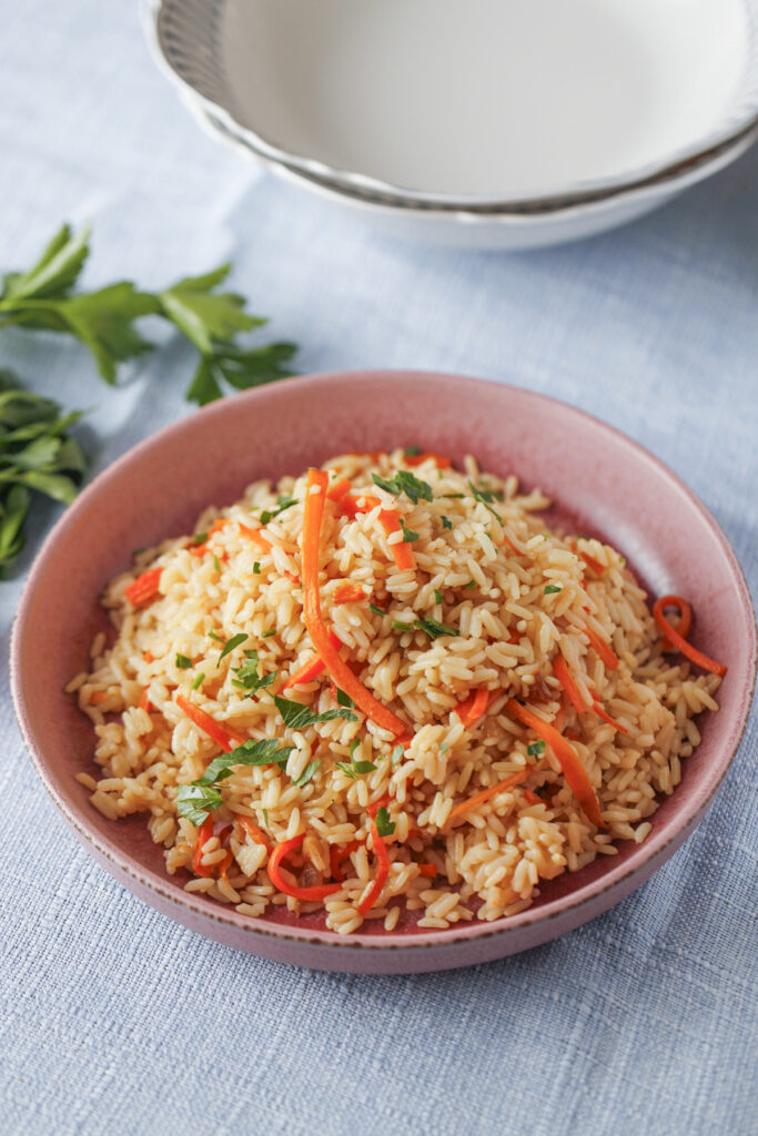 Fluffy carrot and onion pilaf with parboiled rice garnished with fresh parsley.